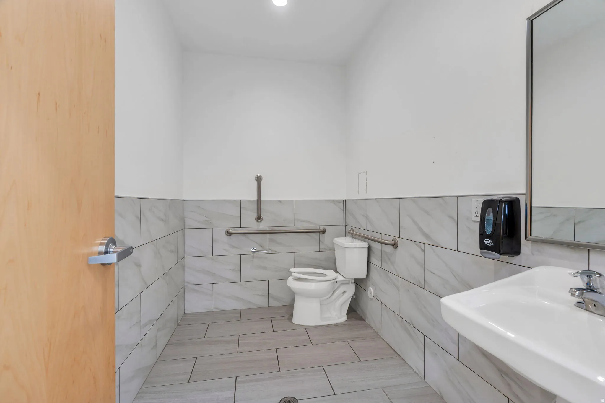 Half bath featuring tile walls, recessed lighting, light tile patterned flooring, and wainscoting