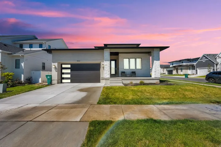 Modern home featuring a porch, driveway, stone siding, an attached garage, and a lawn