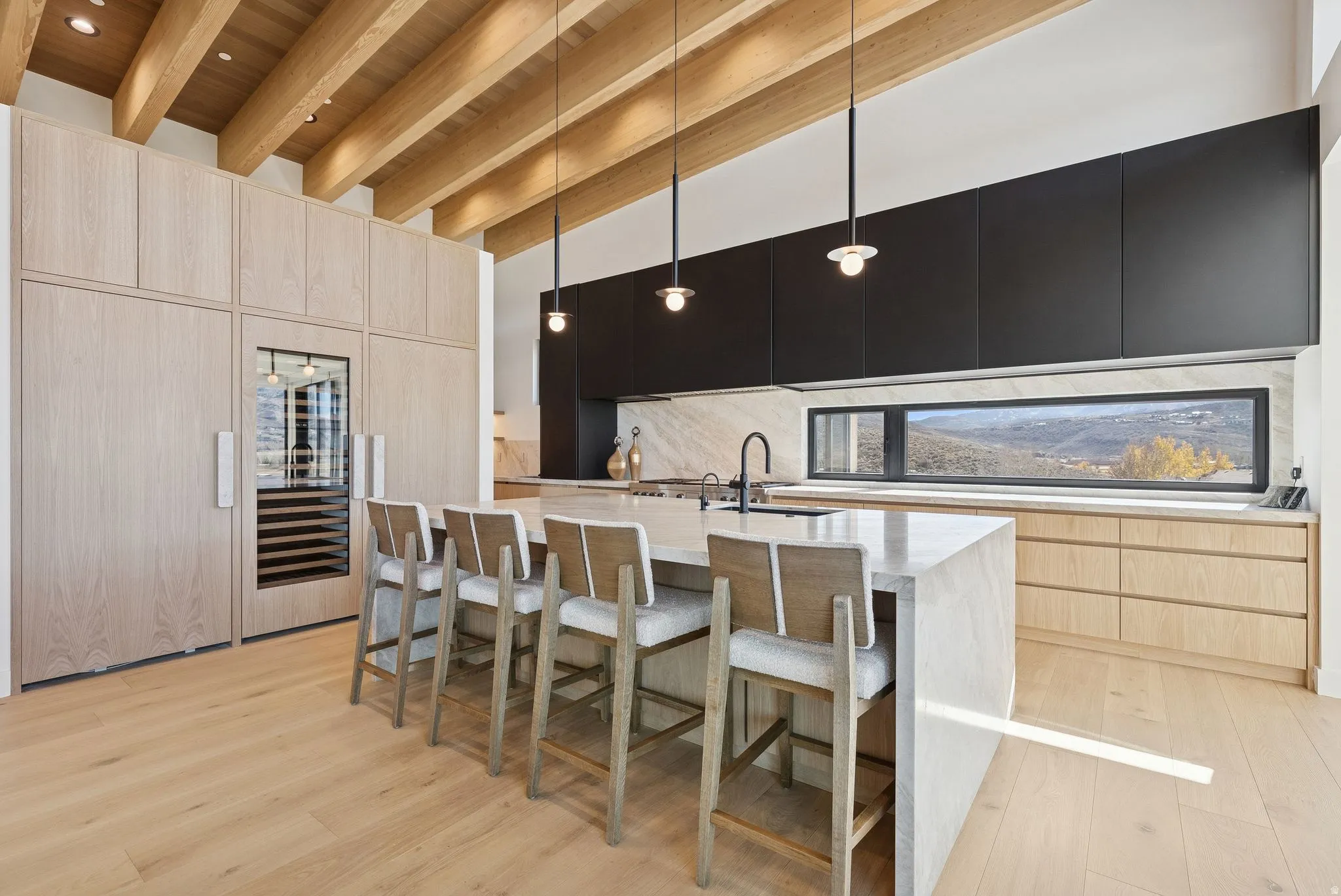 Kitchen featuring light brown cabinets, modern cabinets, dark cabinets, a kitchen bar, and light stone counters