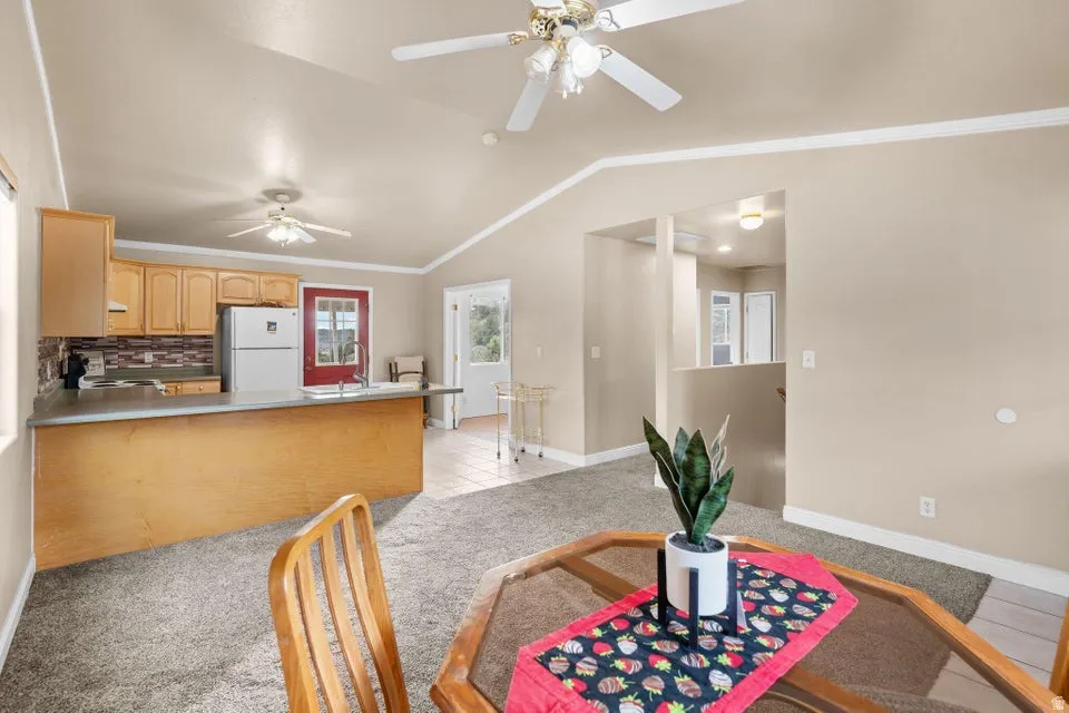 Dining space with vaulted ceiling, ornamental molding, light tile patterned flooring, and light colored carpet