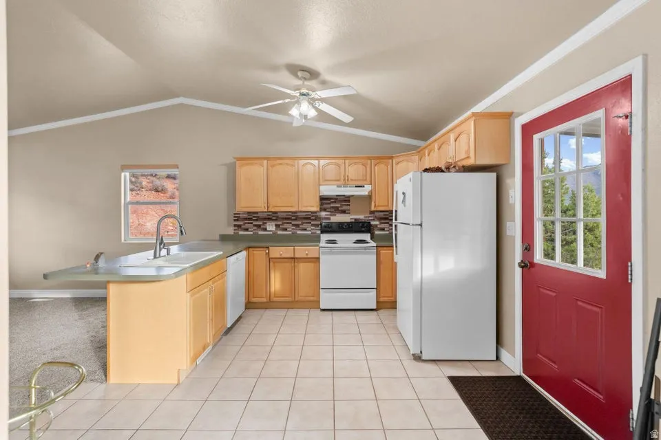 Kitchen featuring white appliances, plenty of natural light, vaulted ceiling, light brown cabinets, and crown molding