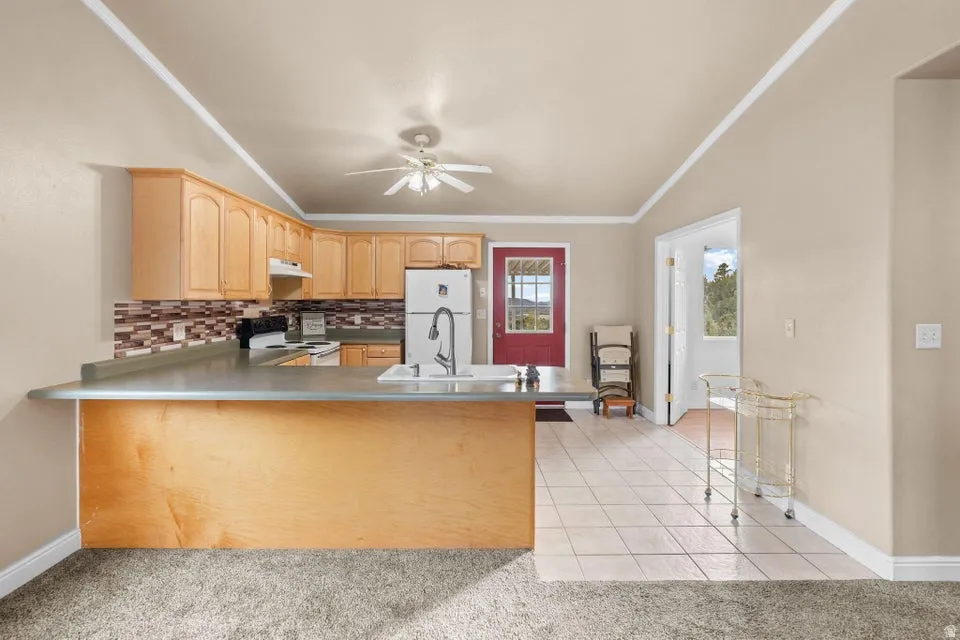 Kitchen featuring light tile patterned floors, light brown cabinets, tasteful backsplash, a peninsula, and freestanding refrigerator