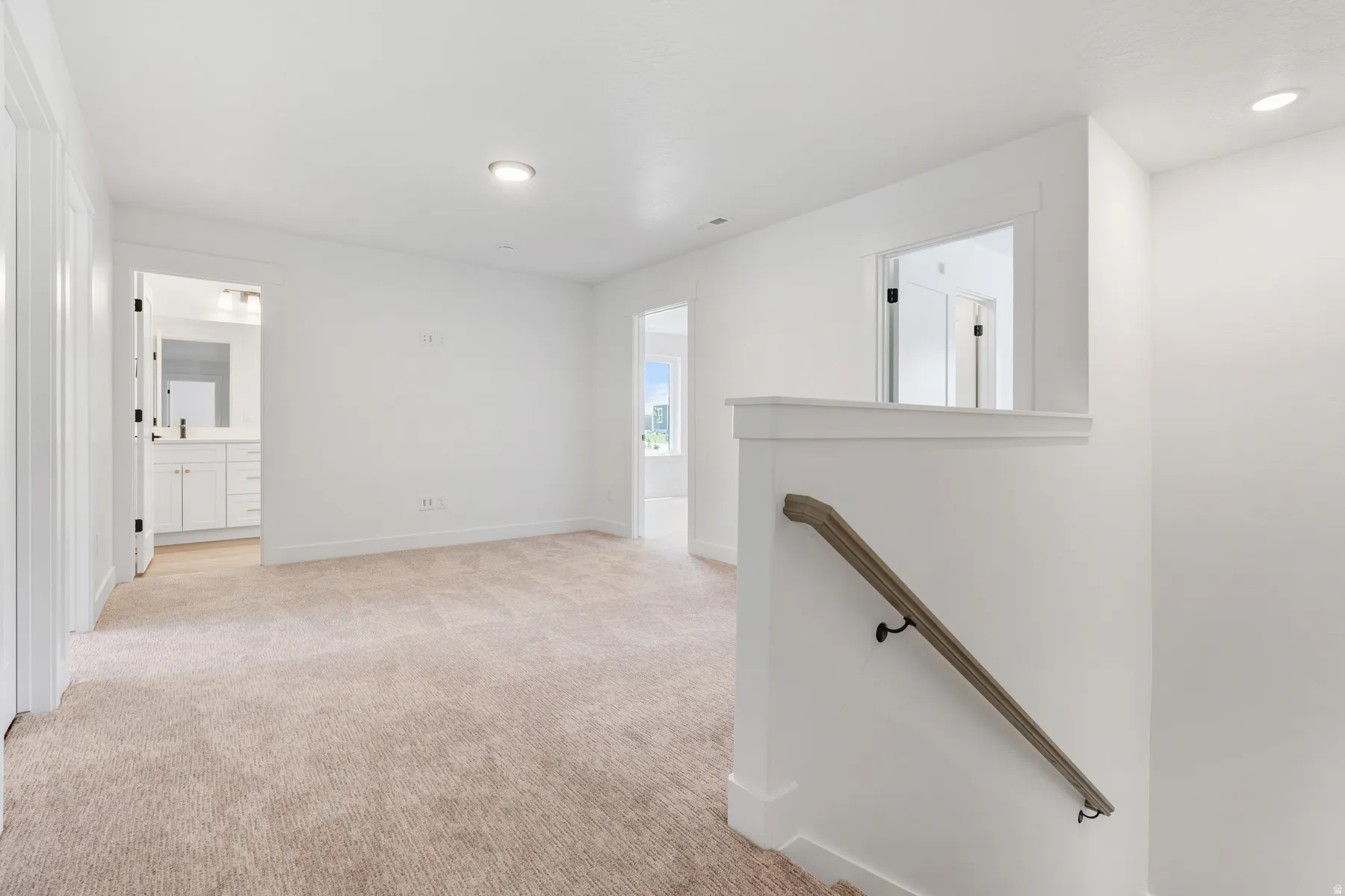 Hallway with an upstairs landing, light colored carpet, and recessed lighting