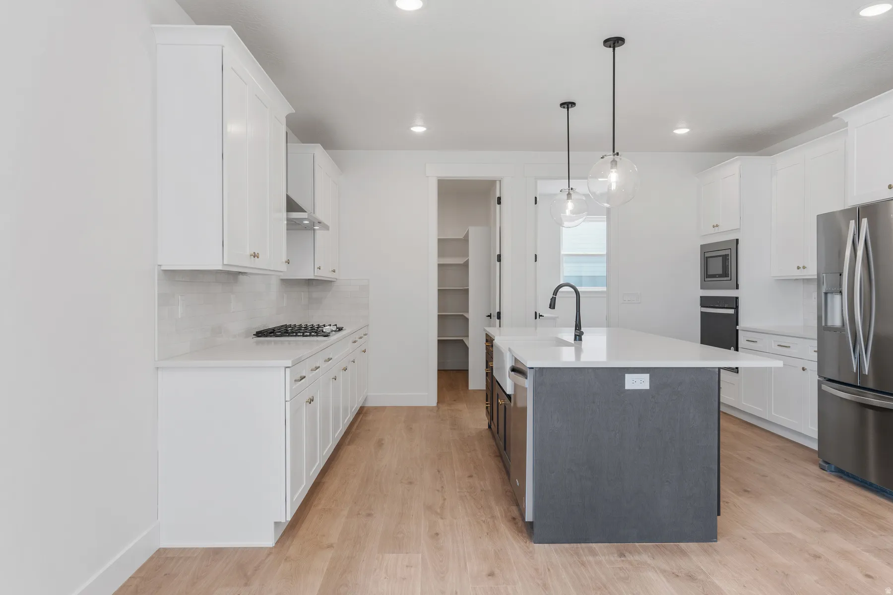 Kitchen featuring white cabinetry, backsplash, light wood finished floors, pendant lighting, and appliances with stainless steel finishes