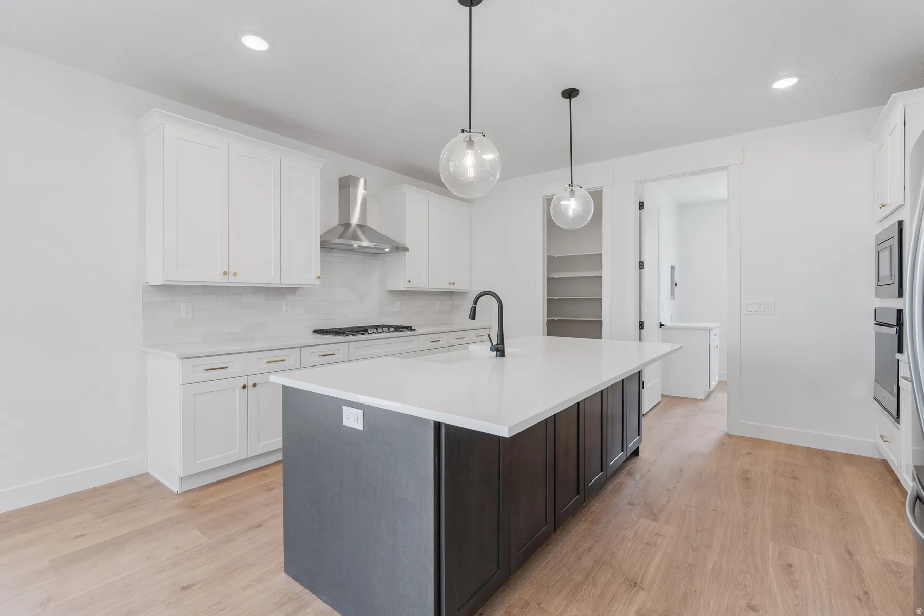 Kitchen with backsplash, white cabinets, an island with sink, light wood finished floors, and recessed lighting