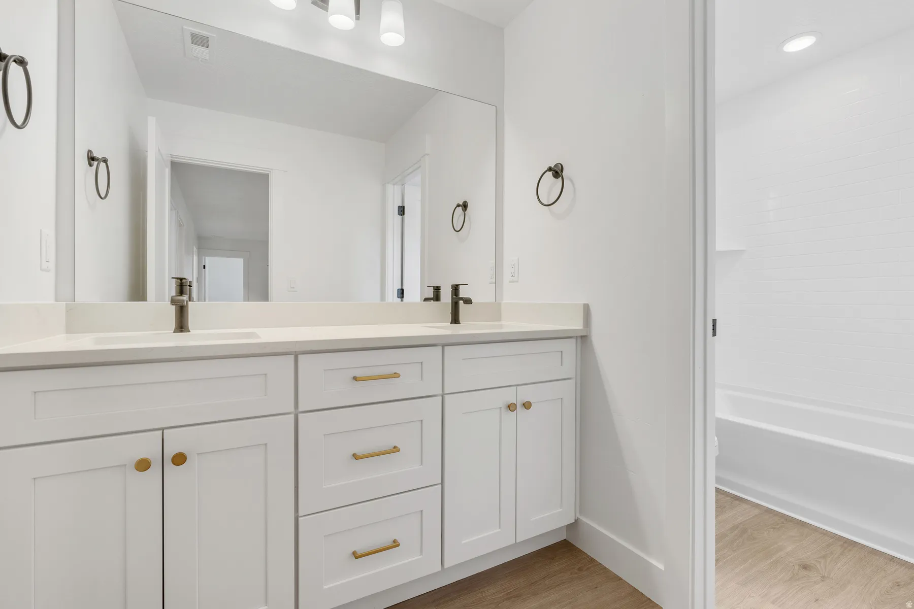 Full bath with double vanity, light wood-style floors, and shower / washtub combination
