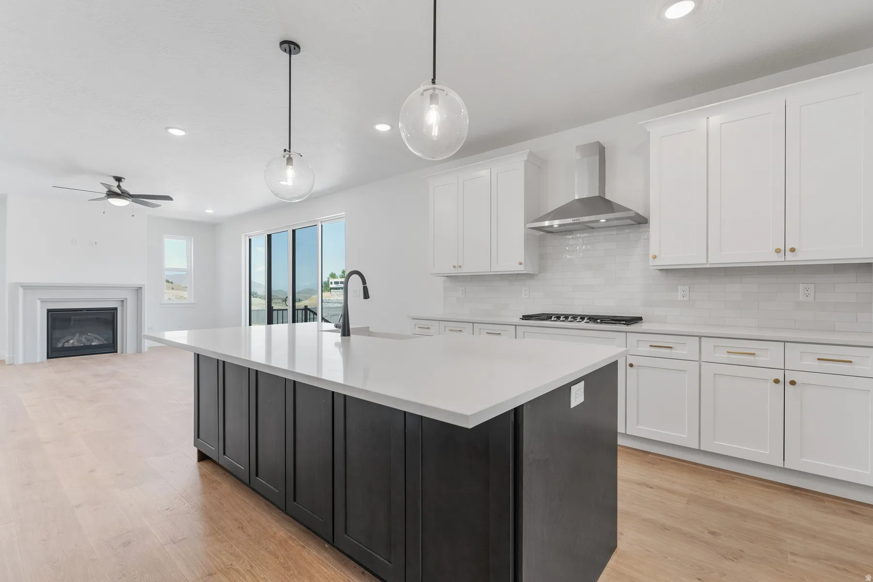 Kitchen featuring white cabinets, decorative light fixtures, wall chimney range hood, light wood-style flooring, and recessed lighting