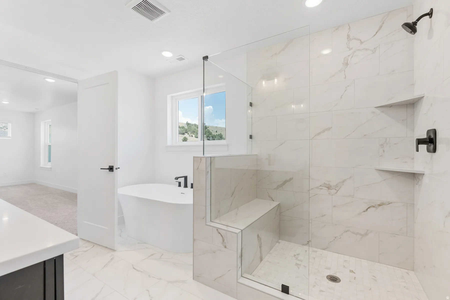 Bathroom featuring a freestanding bath, a marble finish shower, recessed lighting, light marble finish floors, and vanity