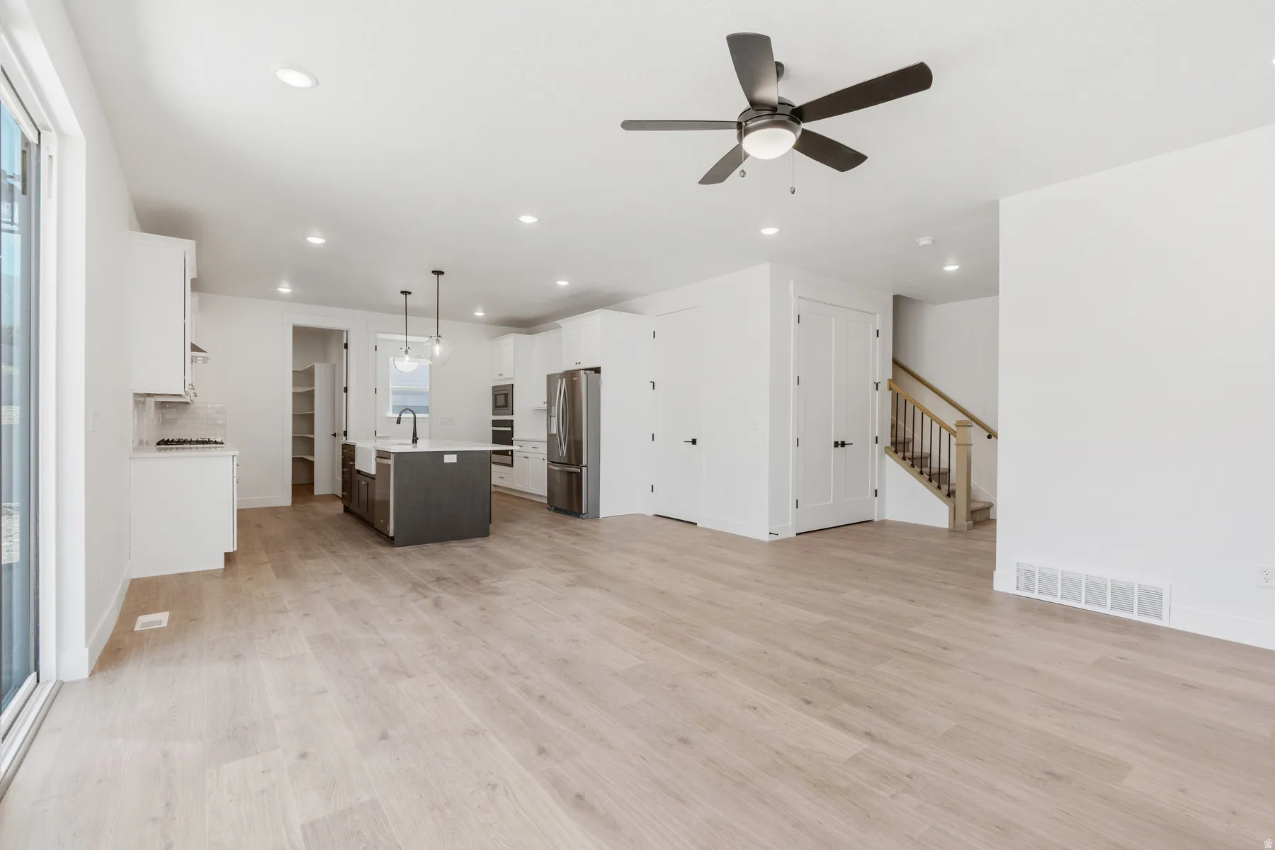 Unfurnished living room featuring light wood-style floors, recessed lighting, ceiling fan, and stairway