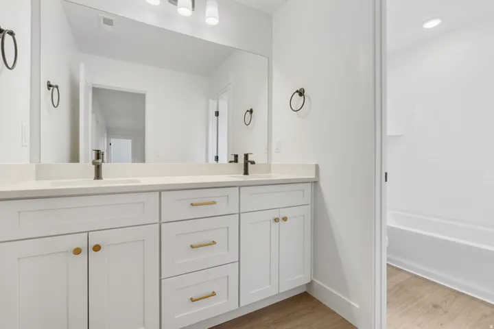 Full bath with double vanity, light wood-style floors, and shower / washtub combination