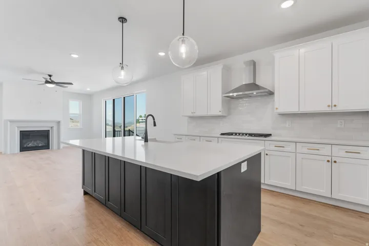 Kitchen featuring white cabinets, decorative light fixtures, wall chimney range hood, light wood-style flooring, and recessed lighting