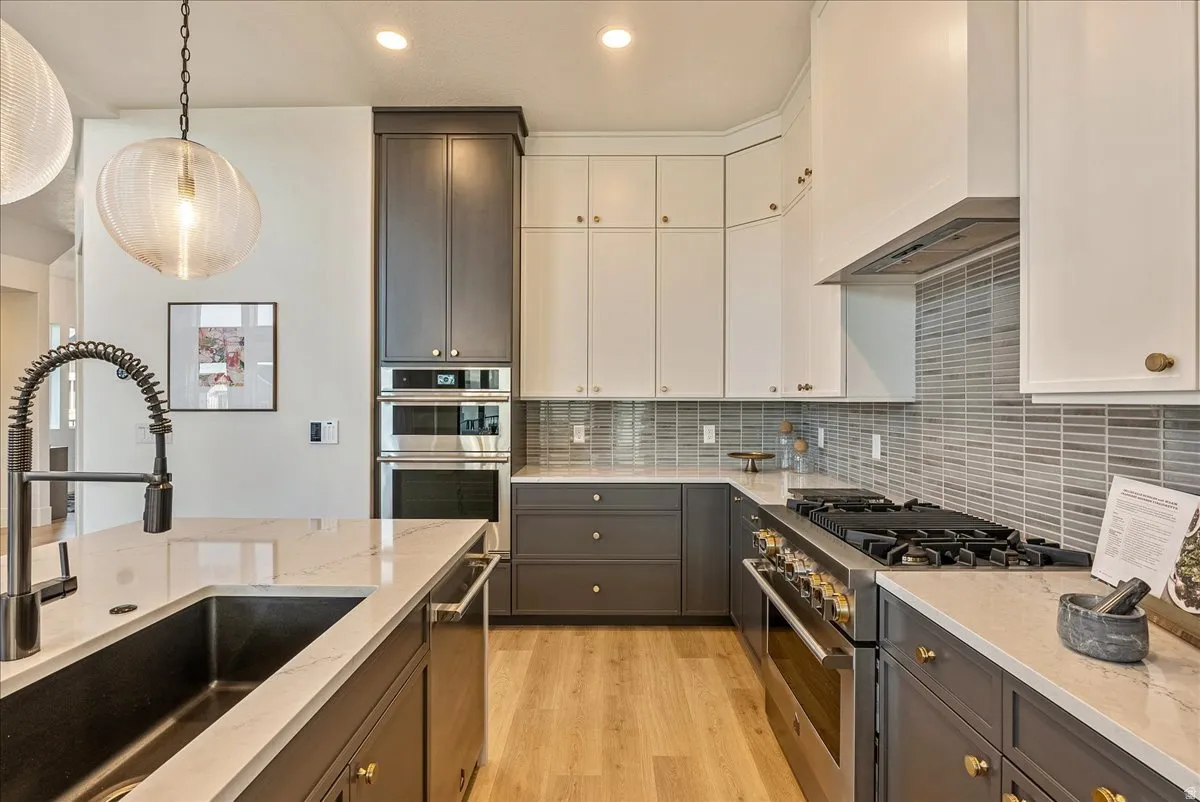 Kitchen featuring stainless steel appliances, decorative backsplash, light stone countertops, light wood-style flooring, and white cabinetry