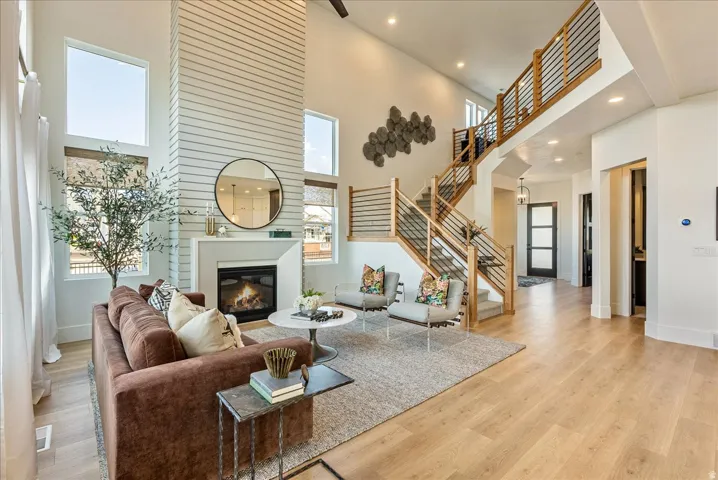 Living area featuring a towering ceiling, light wood finished floors, recessed lighting, a glass covered fireplace, and stairway
