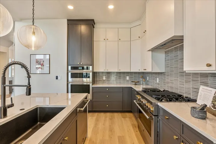 Kitchen featuring stainless steel appliances, decorative backsplash, light stone countertops, light wood-style flooring, and white cabinetry