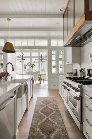 Kitchen featuring appliances with stainless steel finishes, range hood, beamed ceiling, white cabinetry, and light stone countertops