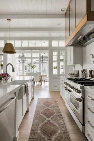 Kitchen featuring stainless steel appliances, range hood, beamed ceiling, light stone counters, and white cabinets