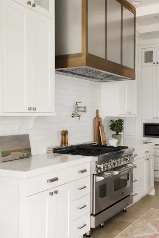 Kitchen featuring custom range hood, stainless steel appliances, glass insert cabinets, white cabinets, and tasteful backsplash