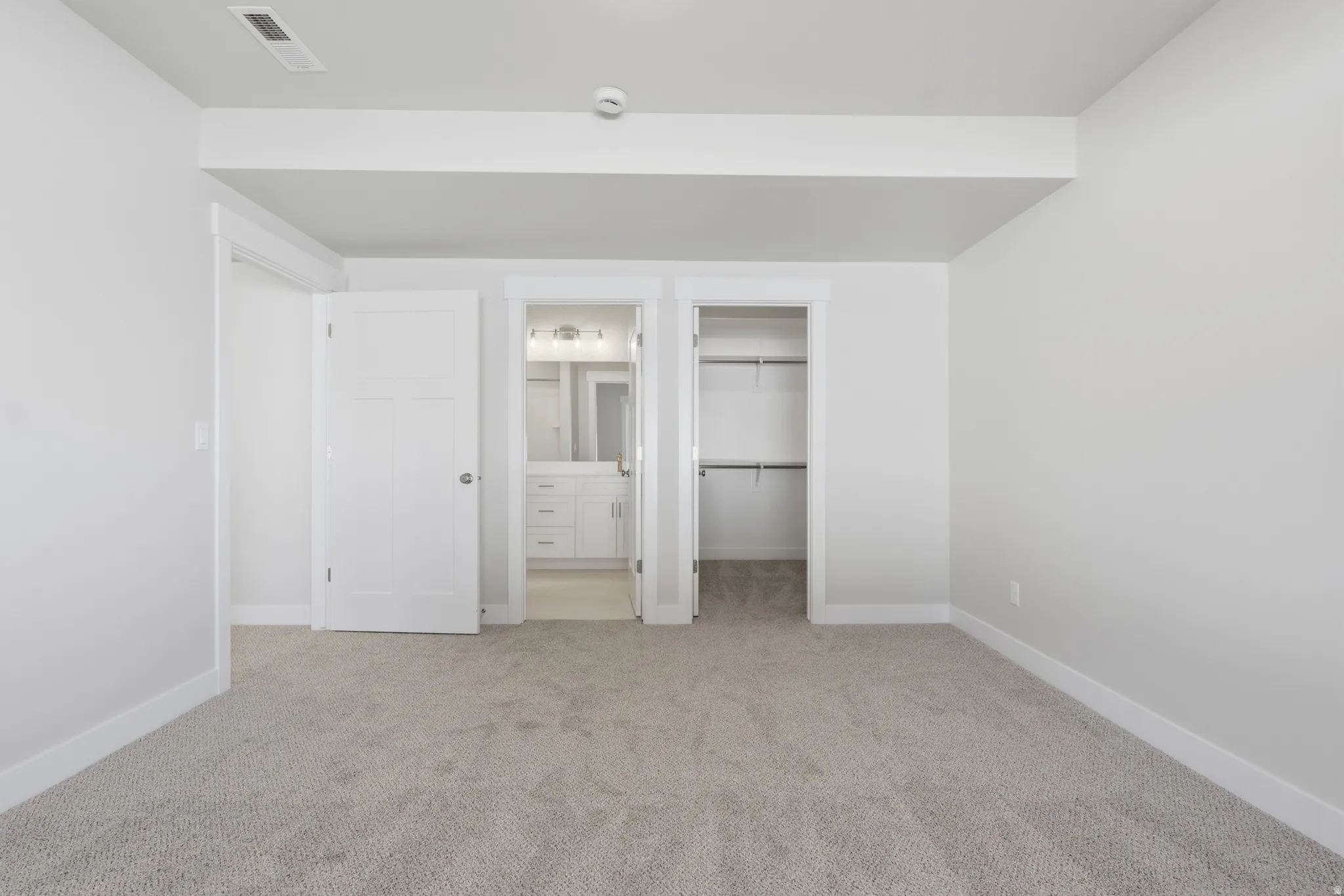 Unfurnished bedroom featuring connected bathroom, a walk in closet, and light colored carpet