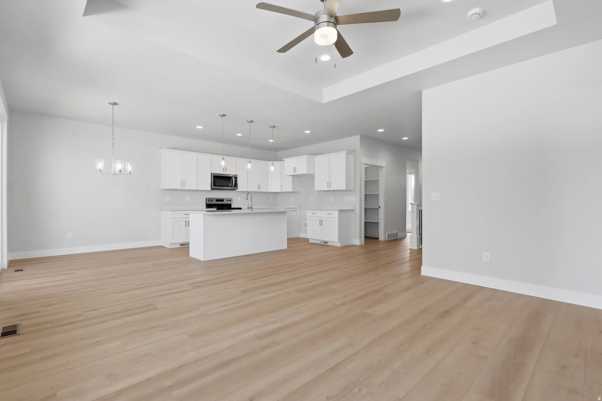 Unfurnished living room featuring a tray ceiling, hanging lights, light wood finished floors, and ceiling fan