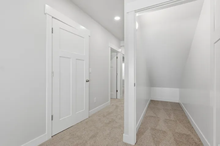 Hallway with light colored carpet and lofted ceiling