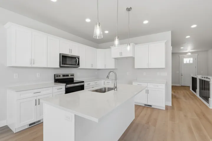 Kitchen featuring stainless steel appliances, white cabinets, a kitchen island with sink, light stone counters, and light wood-style floors