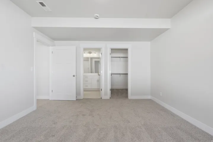Unfurnished bedroom featuring connected bathroom, a walk in closet, and light colored carpet