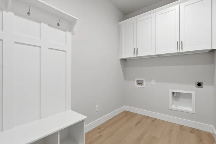 Laundry area with light wood-style flooring, hookup for a washing machine, electric dryer hookup, and cabinet space
