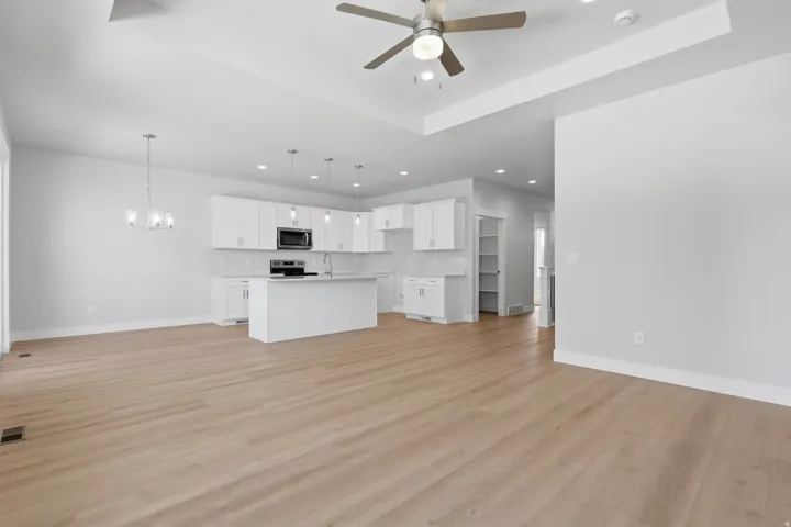 Unfurnished living room featuring a tray ceiling, hanging lights, light wood finished floors, and ceiling fan