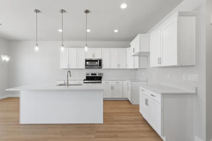 Kitchen with white cabinets, stainless steel appliances, a kitchen island with sink, light wood-style floors, and light stone counters