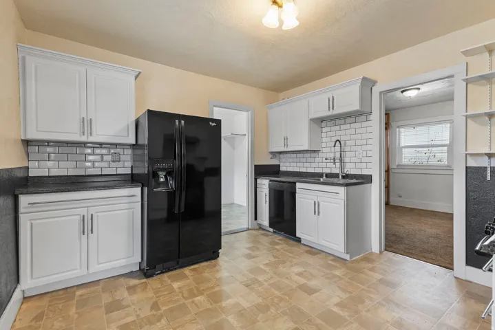 Kitchen with black appliances, white cabinets, tasteful backsplash, and dark stone countertops