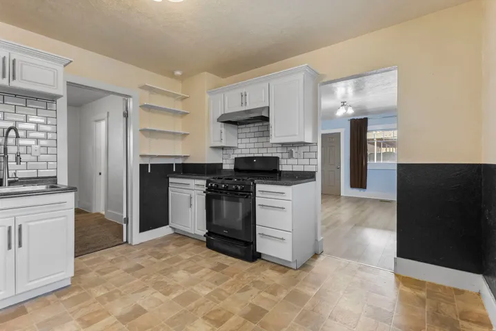 Kitchen featuring black gas range oven, white cabinets, backsplash, under cabinet range hood, and open shelves