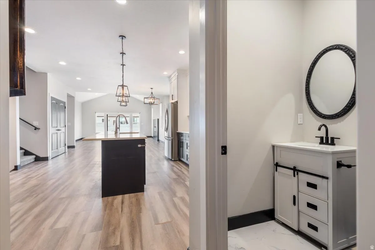 Kitchen with a kitchen island with sink, white cabinetry, pendant lighting, freestanding refrigerator, and vaulted ceiling