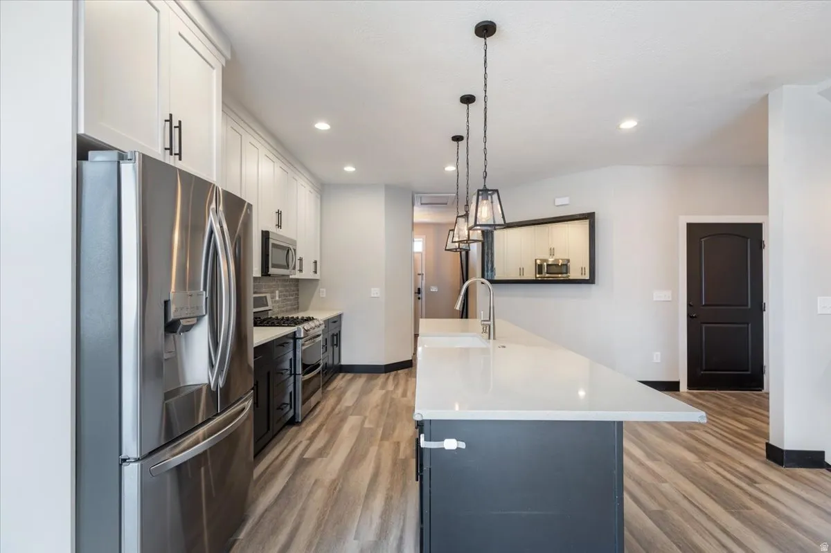 Kitchen featuring appliances with stainless steel finishes, white cabinetry, light wood-style flooring, pendant lighting, and recessed lighting