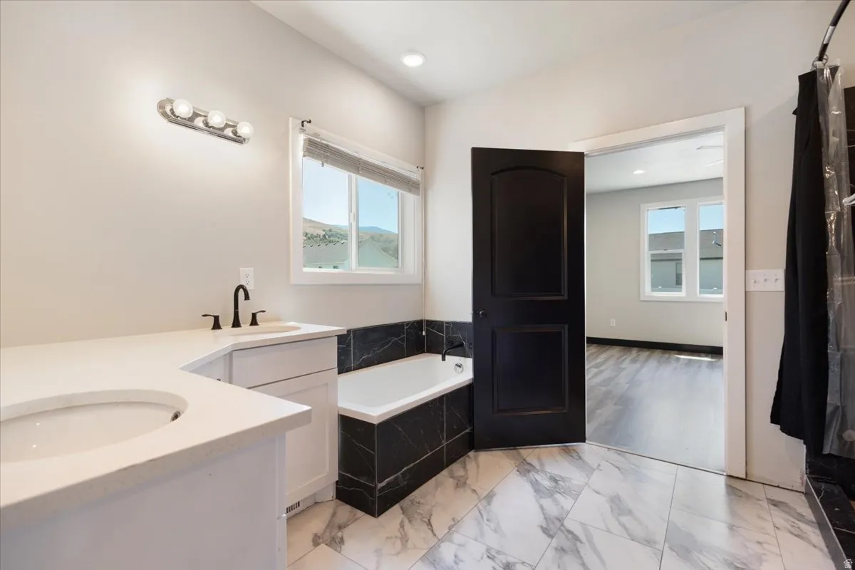 Full bathroom featuring vanity, a bath, light marble finish floors, and recessed lighting