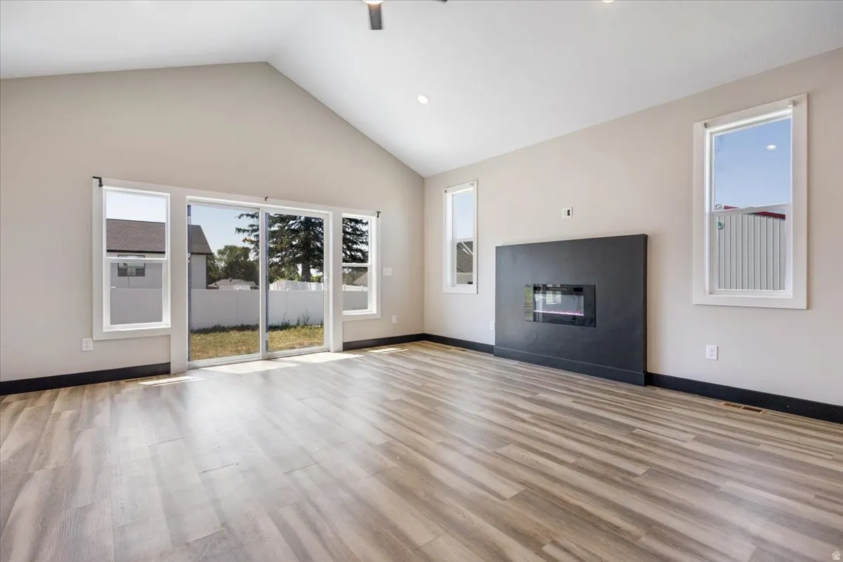 Unfurnished living room featuring light wood finished floors, a glass covered fireplace, high vaulted ceiling, recessed lighting, and a ceiling fan