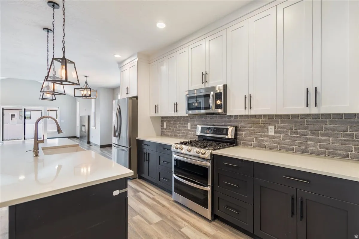 Kitchen featuring white cabinets, appliances with stainless steel finishes, dark cabinets, hanging light fixtures, and tasteful backsplash