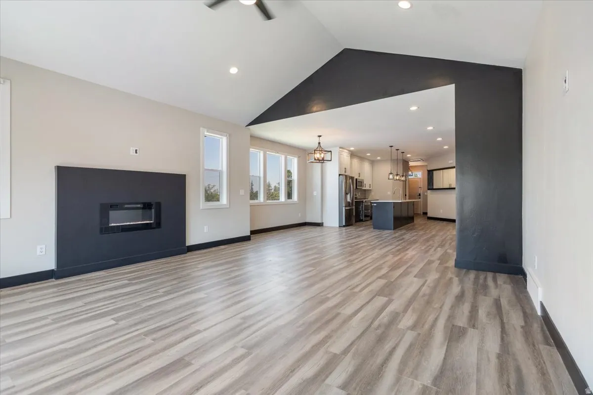 Unfurnished living room with light wood-style floors, recessed lighting, high vaulted ceiling, and a chandelier