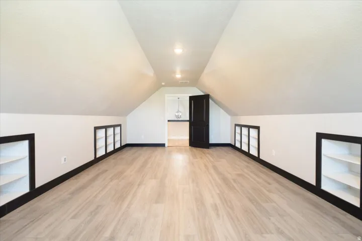 Bonus room featuring light wood-style flooring, lofted ceiling, and a textured ceiling
