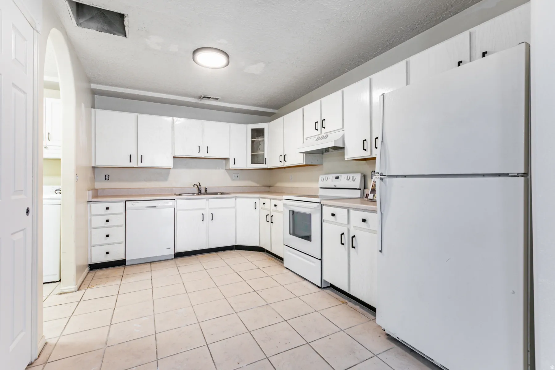 Kitchen featuring white appliances, light countertops, light tile patterned flooring, glass insert cabinets, and white cabinets