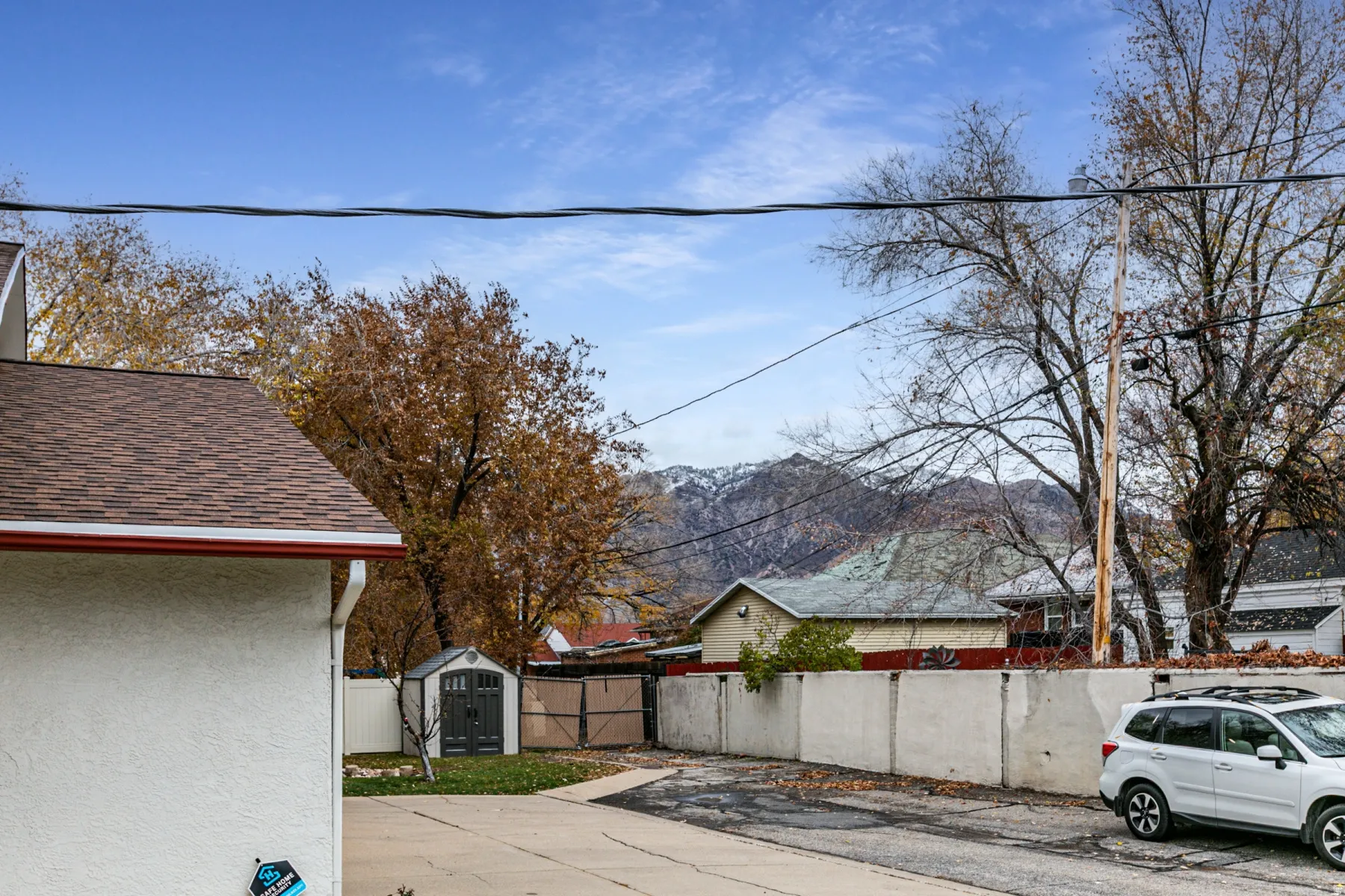 View of property exterior with a storage unit, a mountain view, stucco siding, and a shingled roof