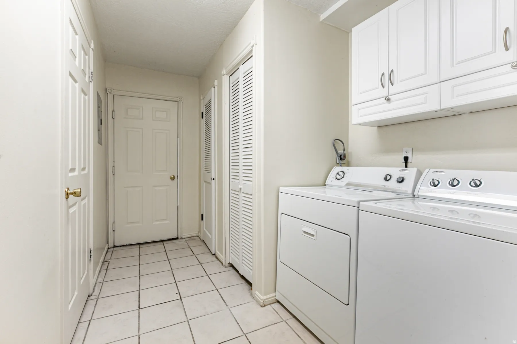 Laundry area with light tile patterned floors, washer and clothes dryer, cabinet space, and a textured ceiling