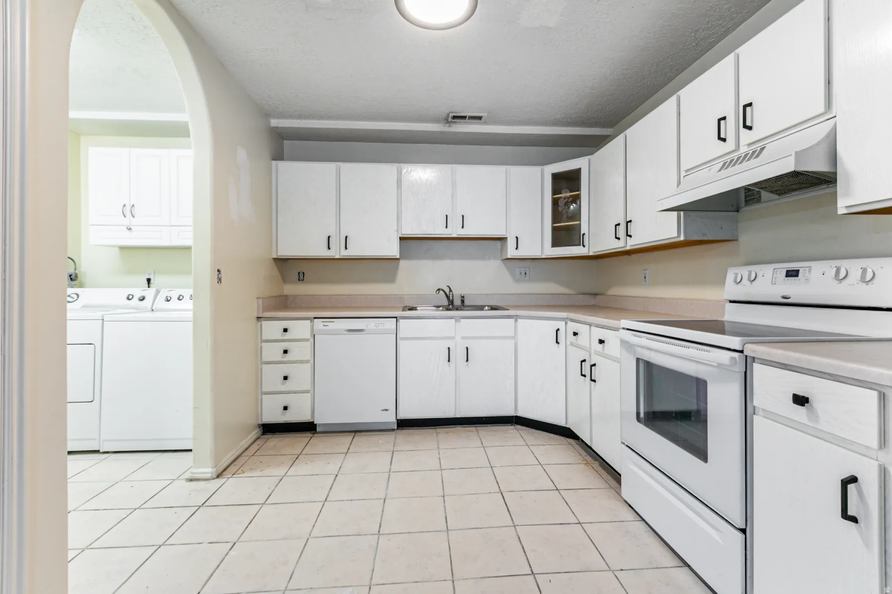 Kitchen with white appliances, under cabinet range hood, arched walkways, light countertops, and light tile patterned floors
