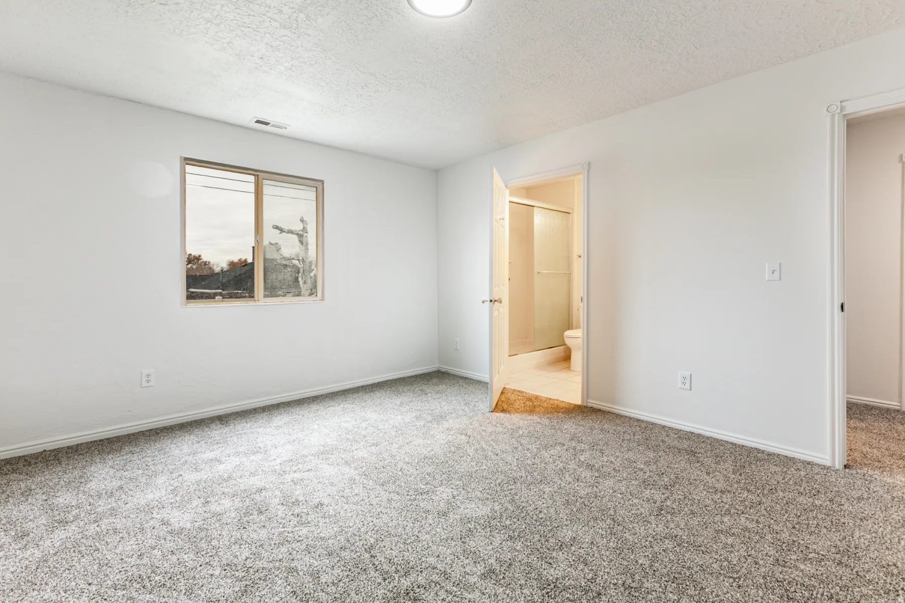 Unfurnished bedroom with a textured ceiling, carpet flooring, and connected bathroom