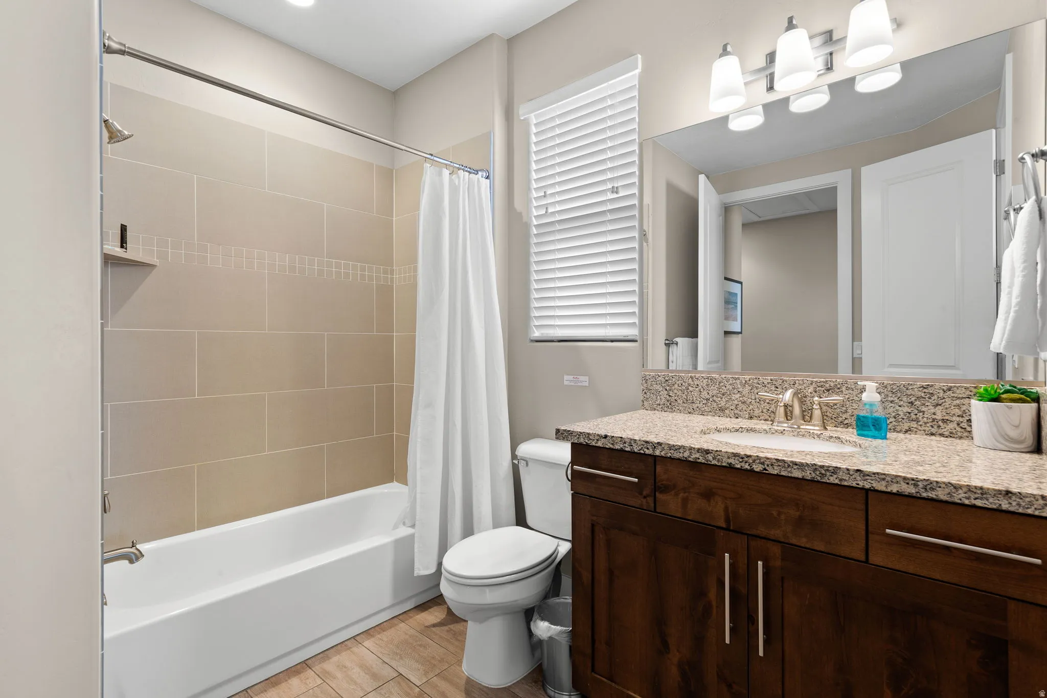Full bath with shower / tub combo, vanity, and light wood-style floors