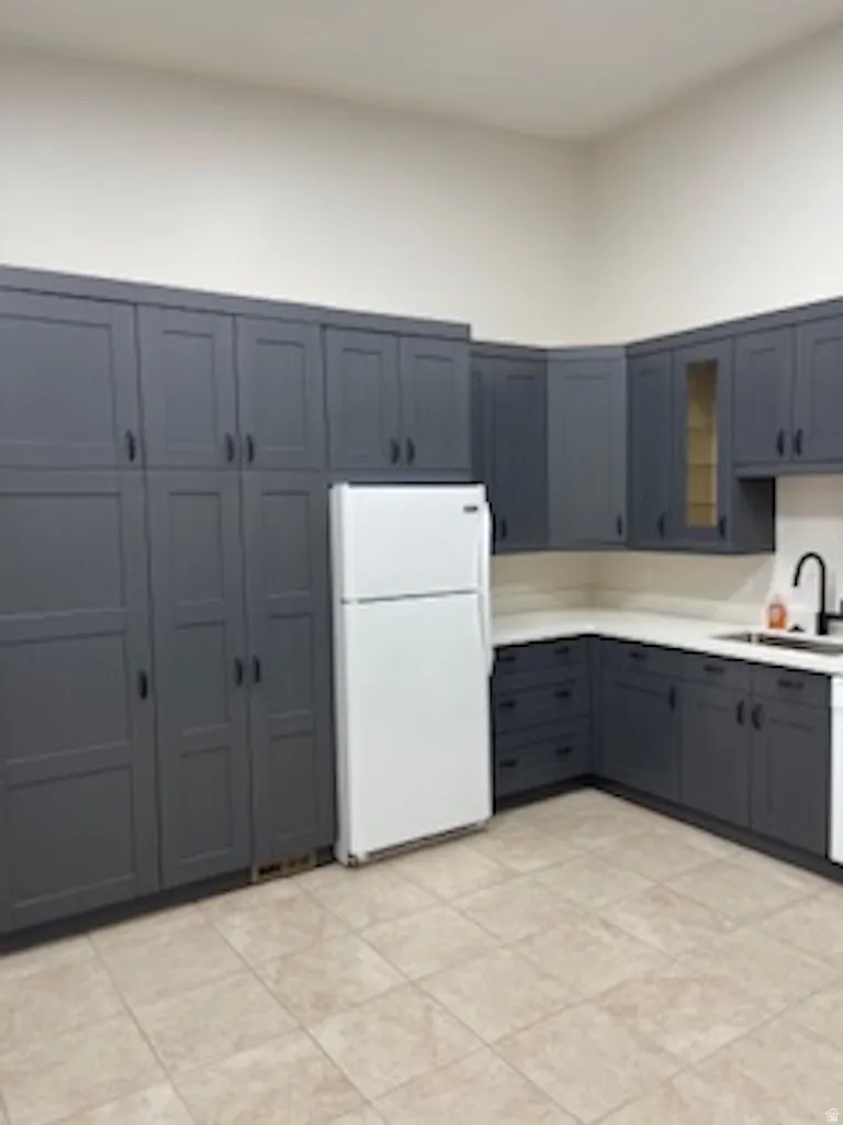 Kitchen featuring glass insert cabinets, freestanding refrigerator, light countertops, and gray cabinets