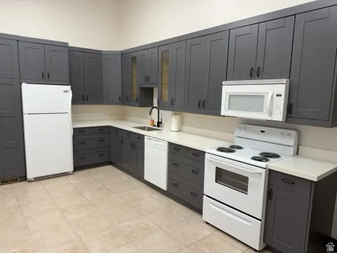 Kitchen with white appliances, gray cabinetry, light countertops, and glass insert cabinets