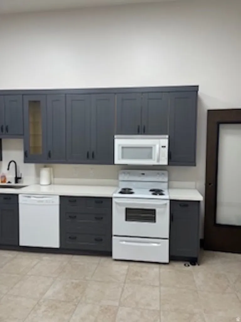 Kitchen featuring white appliances, light countertops, glass insert cabinets, and light tile patterned flooring