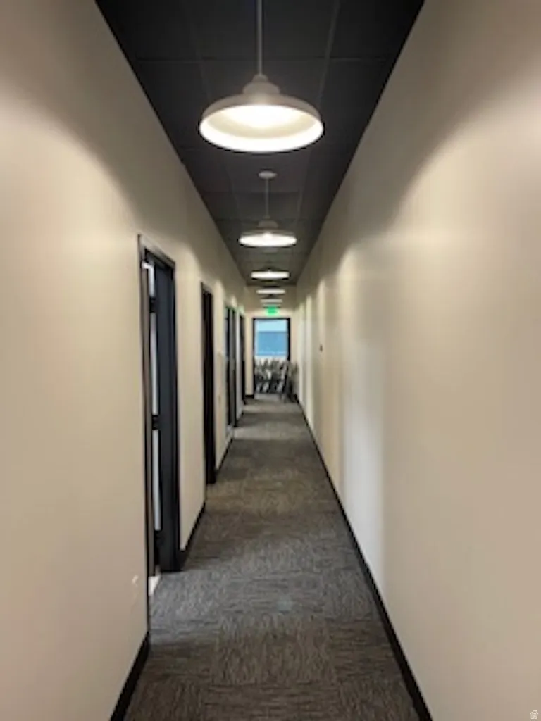 Corridor featuring dark colored carpet and a drop ceiling