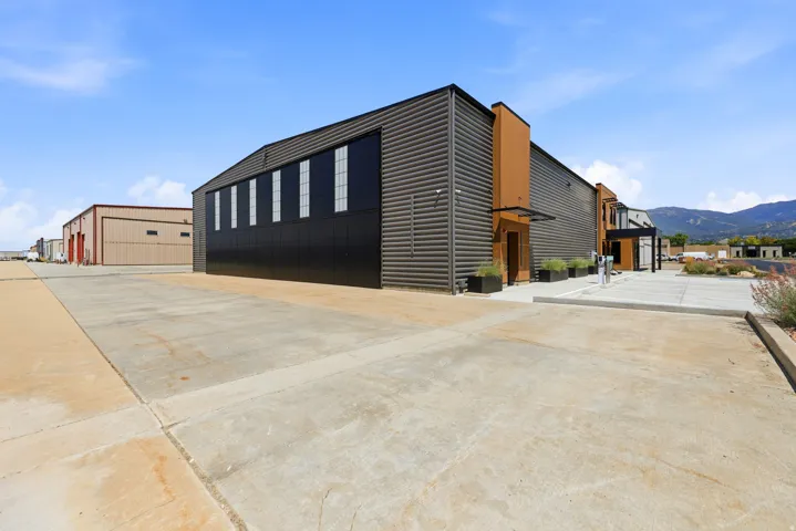 Modern industrial building featuring corrugated metal siding, an expansive concrete pad, large windows, and a covered entryway