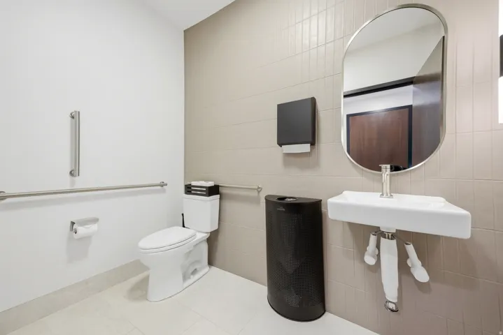Restroom featuring light-toned square wall tiles, a wall-mounted ceramic sink with chrome faucet, and a contemporary oval mirror